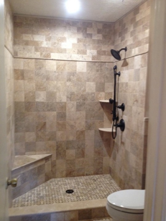 A newly remodeled shower with several aging in place modifications, including a built-in bench, detachable shower head, and built-in storage shelves.