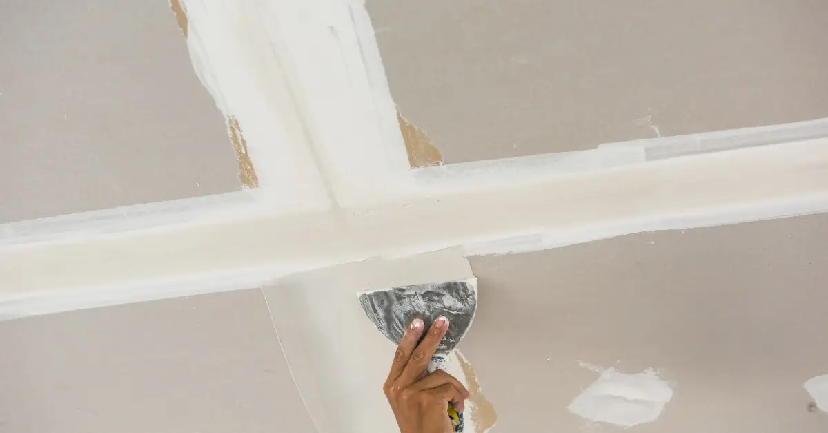 A handyman using a putty knife to spread joint compound over a seam between two new drywall sheets that have been installed on a ceiling during an appointment for ceiling repair in Wichita, KS.