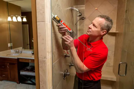 A handyman from Mr. Handyman using a caulking gun to seal the glass shower enclosure of a new shower remodel.