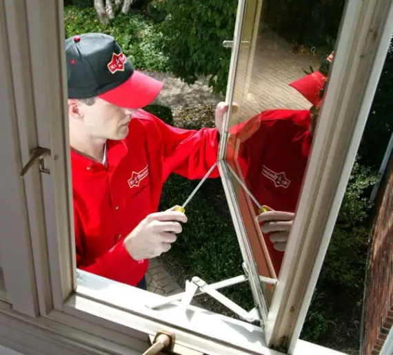 A handyman using a screwdriver to adjust the mechanical components of a casement window during an appointment for window repair in Tulsa, Oklahoma.