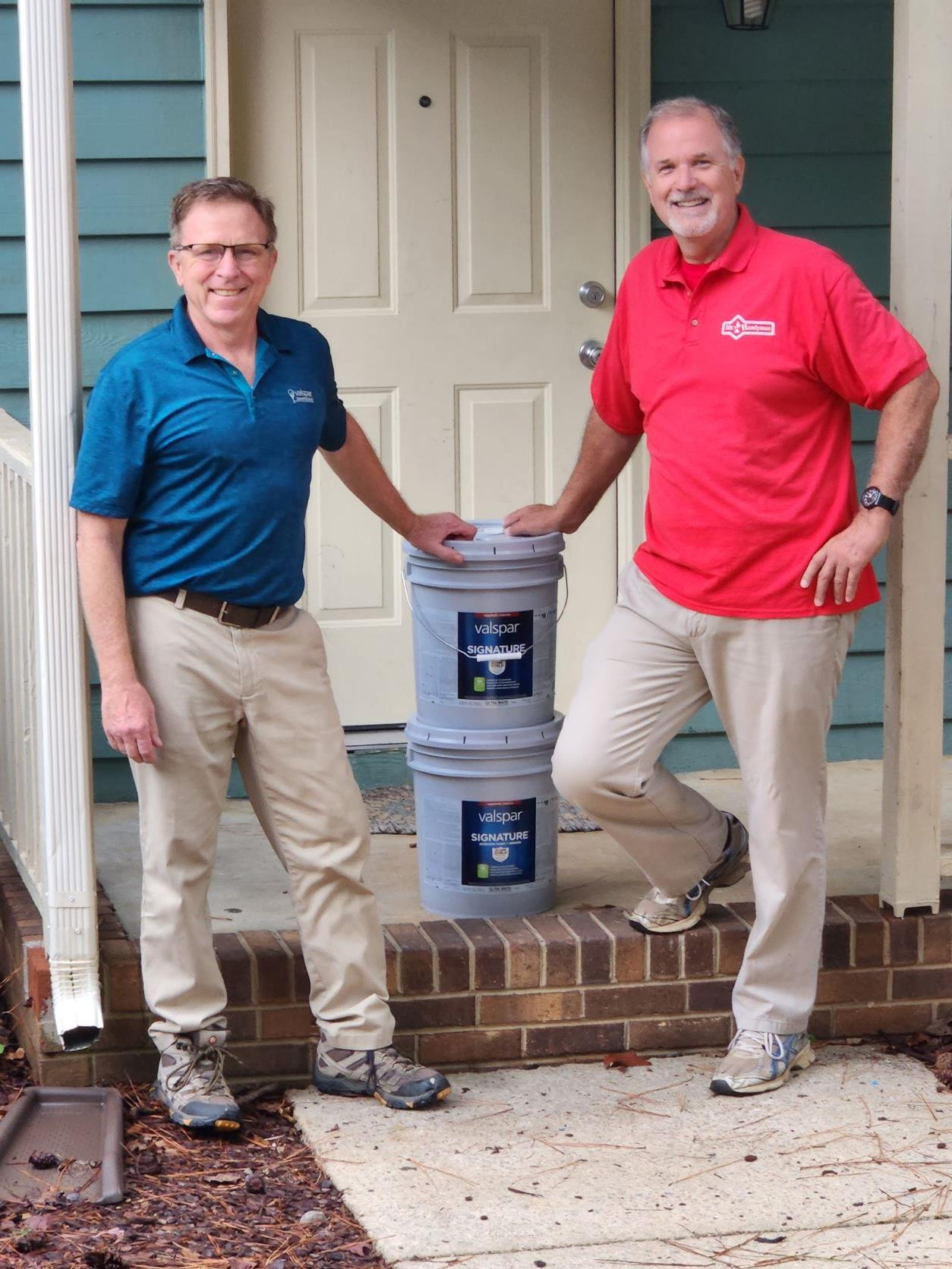 2 persons standing in front a house with paint buckets
