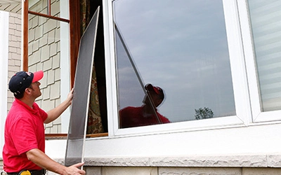 A handyman from Mr. Handyman installing a new window screen for the exterior window of a home.