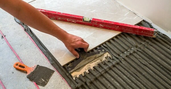 A handyman using a notched trowel to spread mortar across a subfloor while replacing a single tile using a level and putty knife during an appointment for tile repair in Wichita, KS.