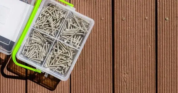 A plastic box with four compartments full of screws used for deck repair sitting on top of a brown wooden deck.
