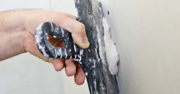 A handyman using a putty knife and joint compound to repair drywall in Brighton, CO.