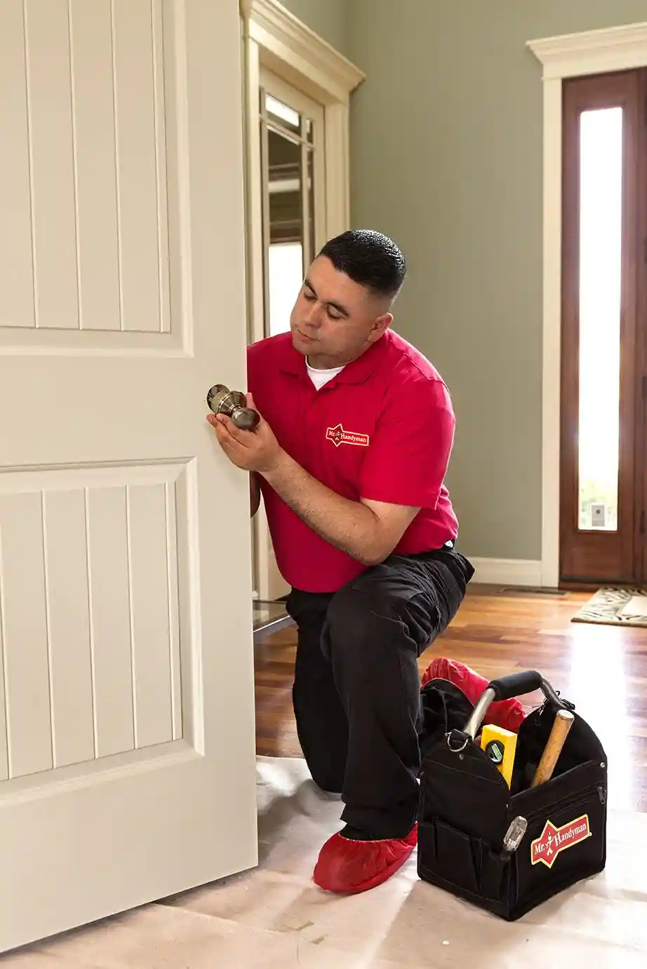 A handyman from Mr. Handyman installing a new doorknob on a bedroom door during an appointment for door repair in Vancouver, WA.