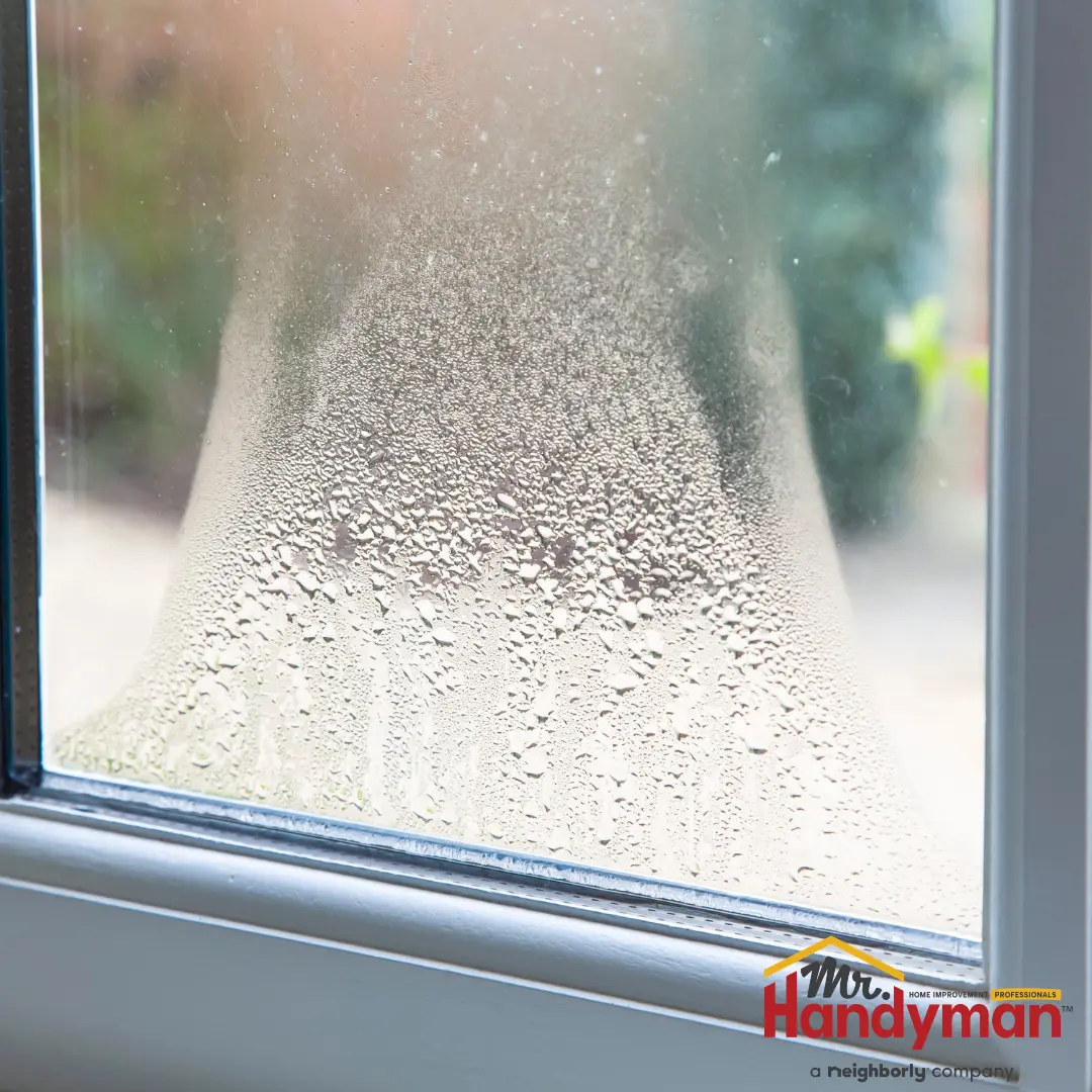 Close-up of a window glass with condensation droplets on the inside, blurring the outdoor view behind it.