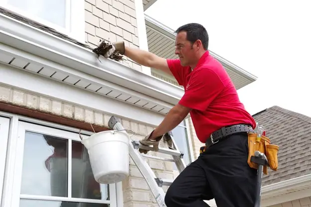  A handyman from Mr. Handyman standing on a ladder and reaching into a home&rsquo;s gutters as he provides service for gutter cleaning in Collinsville, IL.