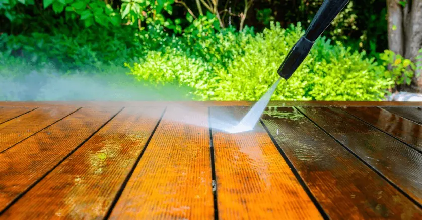  A close-up of the nozzle on a power washing machine as it&rsquo;s used to clean a wooden deck by blasting it with high-pressure water.