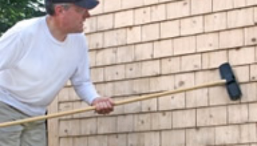 Homeowner cleaning exterior wood siding with a long-handle brush.