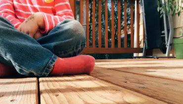 Kid sitting cross-legged on a wooden deck.