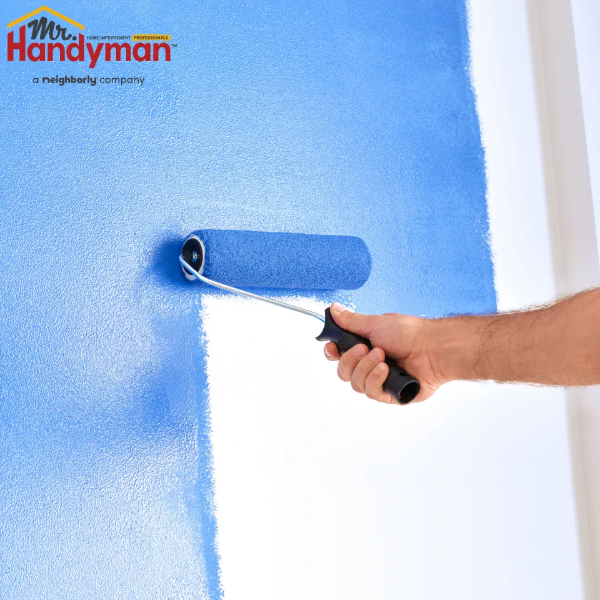Person applying blue paint to a wall using a roller.