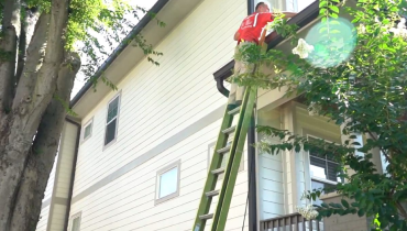 Mr. Handyman technician cleaning house gutters on a ladder during a professional home maintenance service.