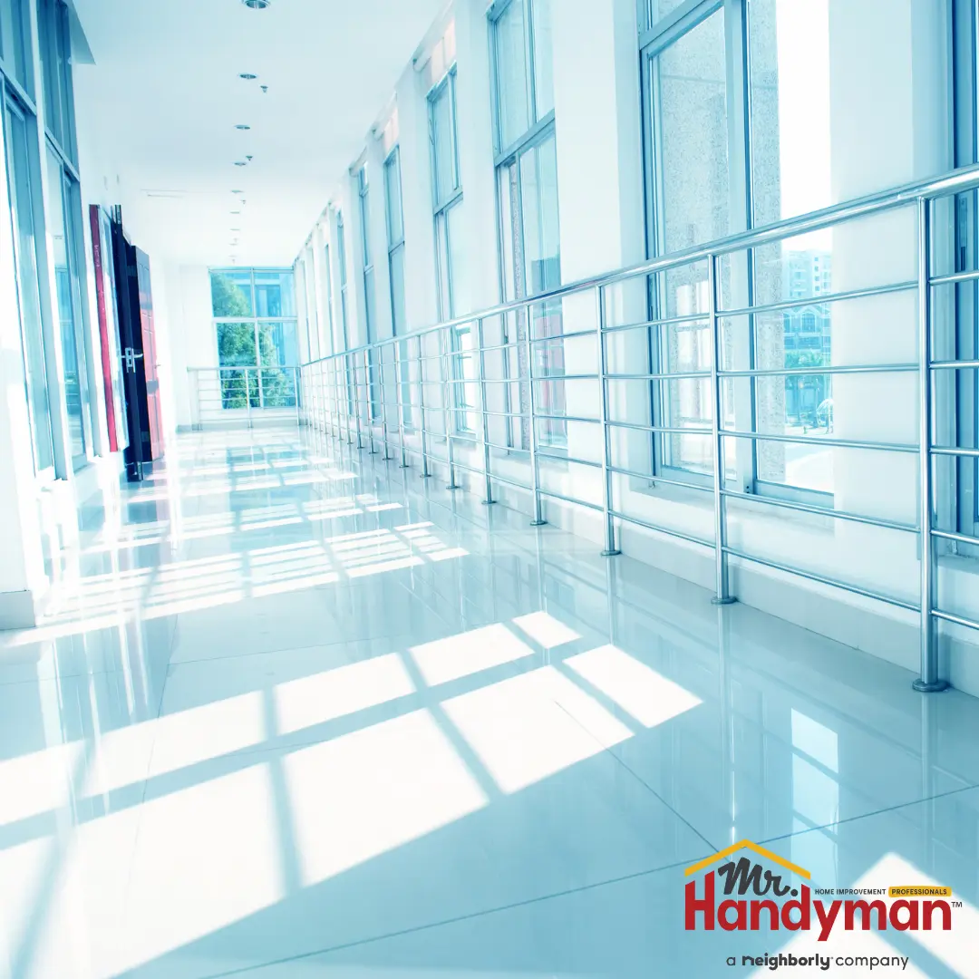 A bright, modern hallway with large windows and reflective floors, bathed in natural light.
