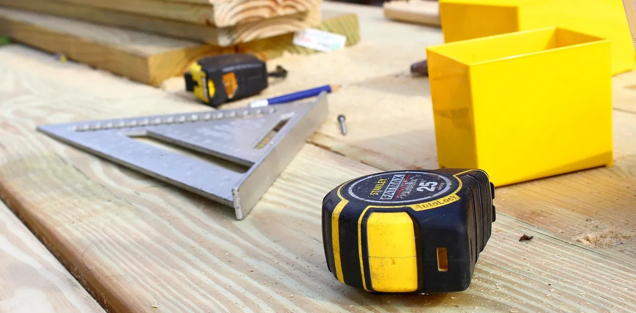 Tape measures, a carpentry square and other tools used for finish carpentry in Frisco, TX laying on top of wooden boards.