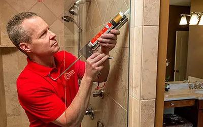 Mr. Handyman service professional caulking the glass of a shower door.