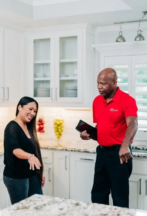 A Mr. Handyman technician holding a tablet and discussing a kitchen counter remodel with a client.
