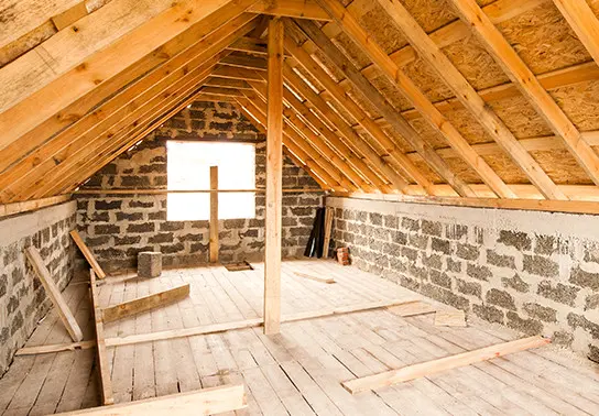 Unfinished attic with exposed brick and pieces of wood on the floor.