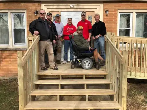 Mr. Handyman of Waukesha team poses with veteran on newly built stairs and wheelchair ramp at veteran's home.