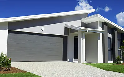 A house painted in shades of gray with a dark gray garage door under a blue sky.