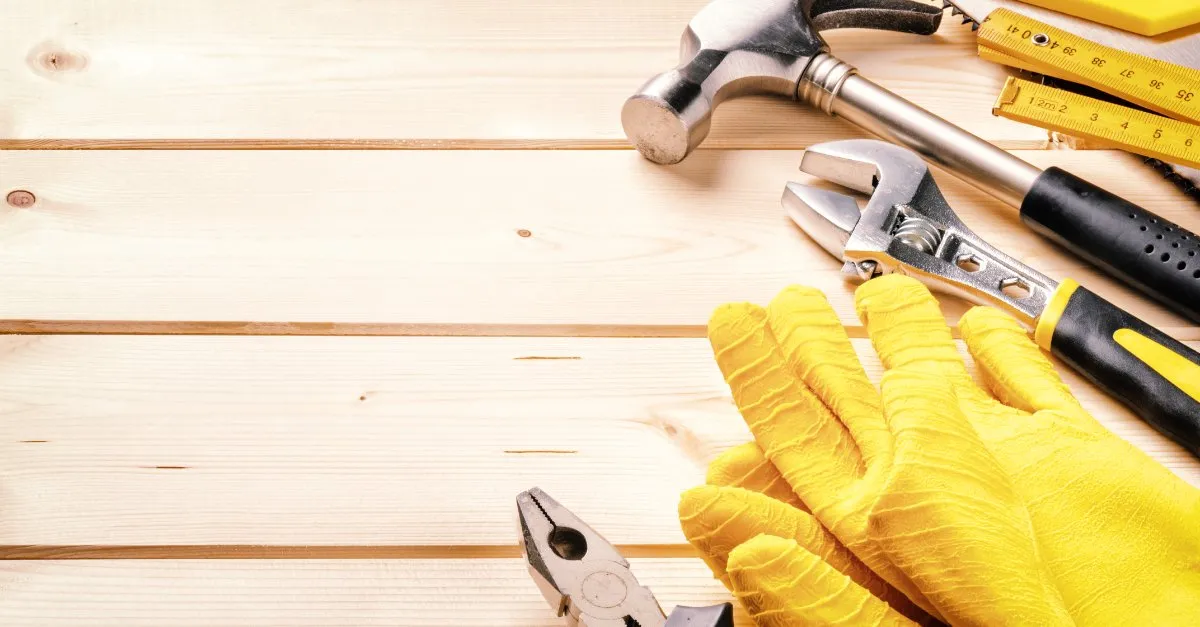 A hammer, adjustable wrench, pair of pliers, set of safety gloves and other tools that would commonly be used by a Montgomery handyman lying on top of wooden boards.