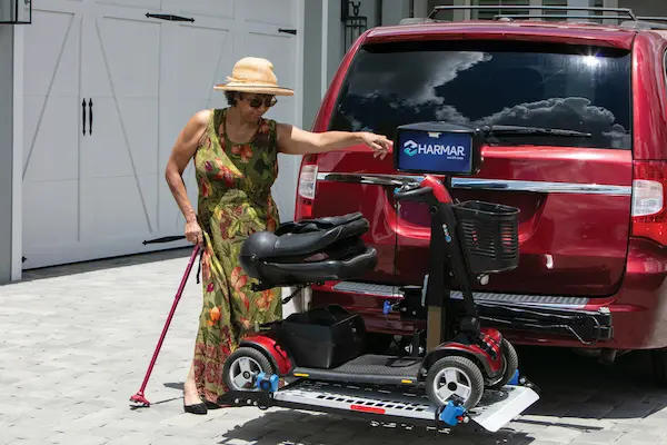 A woman guiding her scooter onto a hitch lift on the back of her vechile.