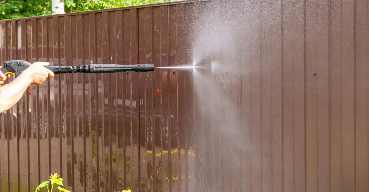 A handyman aiming a pressure washer at a brown fence as it sprays out a jet of water during an appointment for pressure washing in Denton, TX.