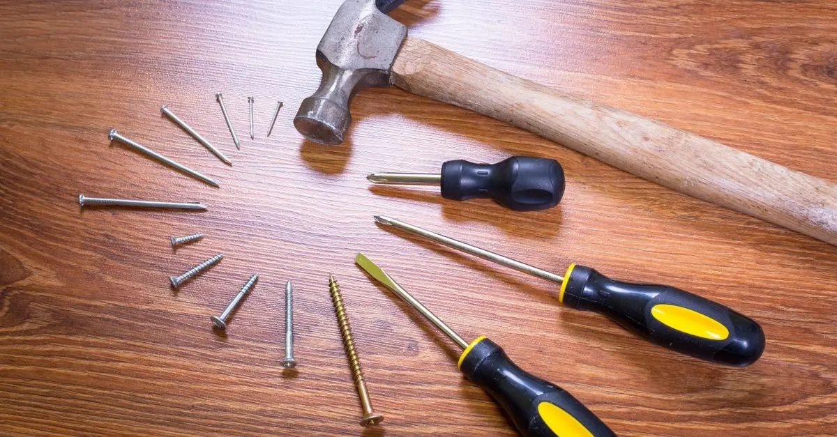 Tools used by a commercial handyman arranged in a circle on a wooden surface, including nails, screws, screwdrivers, and a hammer.